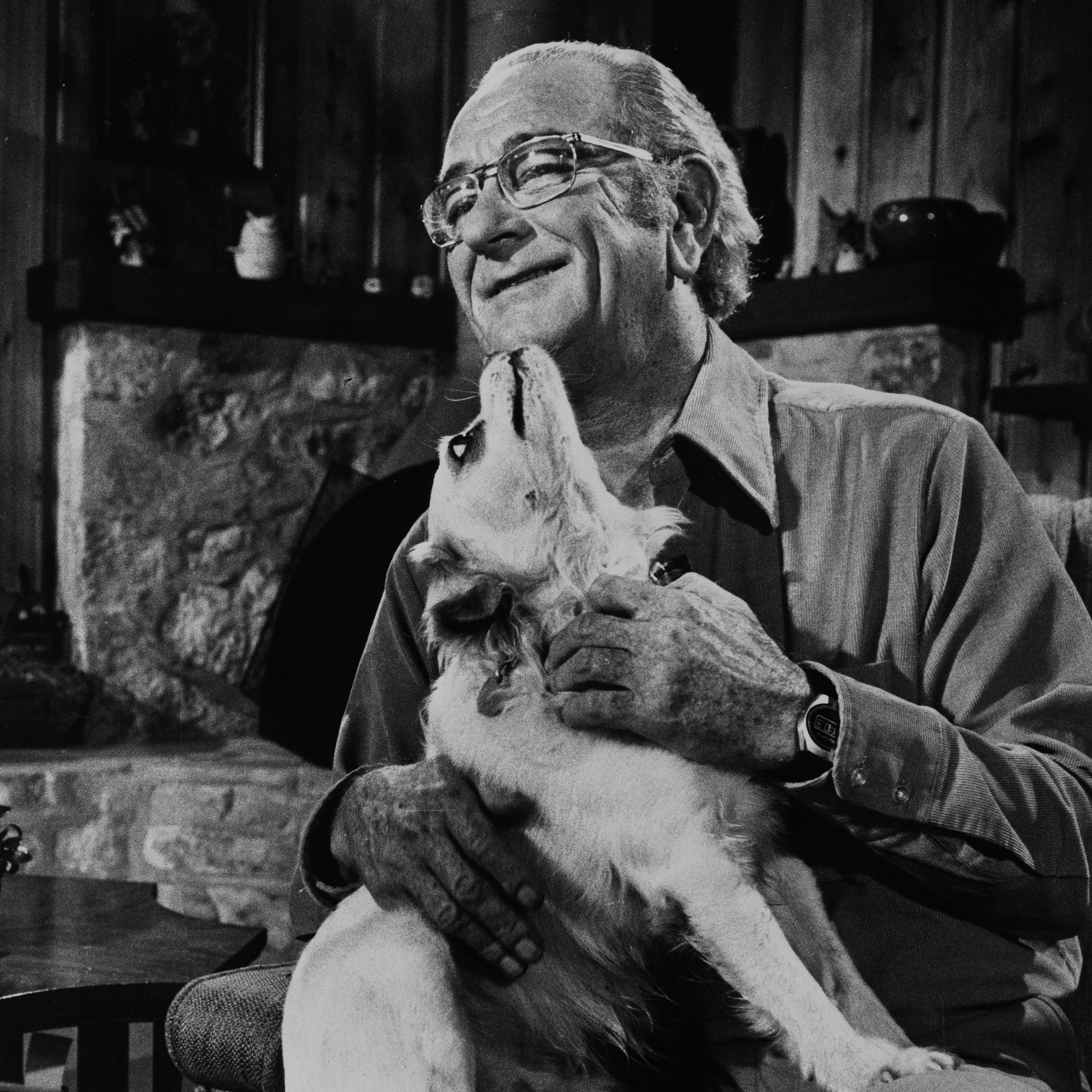 President Johnson, in casual attire and glasses, sits at home with his dog Yuki in his lap. 